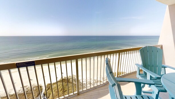 A balcony with a view of the ocean, a sign prohibiting smoking and feeding animals, and two blue chairs.