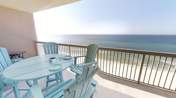 A balcony with a table and chairs, overlooking a beach and the ocean.