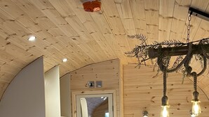 Een gezellige slaapkamer met een bed, een donkere gestoffeerde bank en een houten plafond met zichtbare balken en hangende lampen.