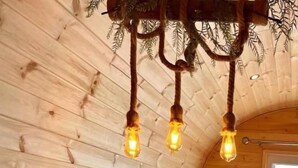 Een houten interieur met een gedekte eettafel voor twee personen, een hanglamp en uitzicht op het landschap.