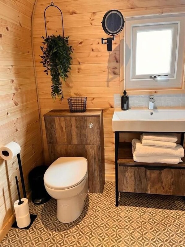 A compact bathroom with a toilet, sink, and hanging plants. - New Farm Holidays (Winsford)