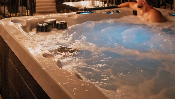 Un jacuzzi con cubierta de madera y luces colgantes, rodeado de árboles.