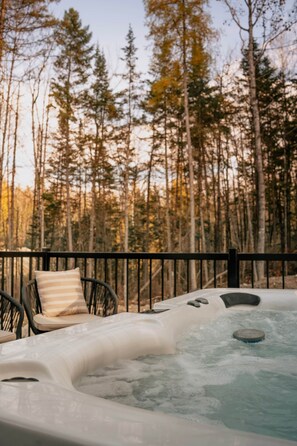 Ein Whirlpool mit Holzterrasse und Stühlen, umgeben von einem Wald.