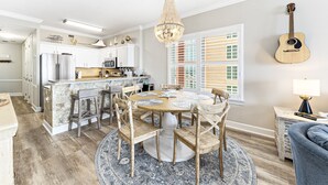 A modern kitchen with a central island, bar stools, and a dining area with a round table and chairs. - "Searenity" A  Luxury Vacation Rental directly on The Beach! (Gulf Shores)