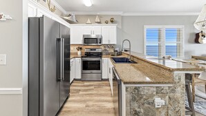 A modern kitchen with stainless steel appliances, white cabinetry, and a granite countertop. - "Searenity" A  Luxury Vacation Rental directly on The Beach! (Gulf Shores)