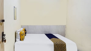Een enkel bed met een witte matras, een deken met blauwe en gele strepen en een stippenbekken.