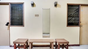 Een gang met twee houten banken, een deur met een metalen hendel en een raam met een metalen traliewerk.