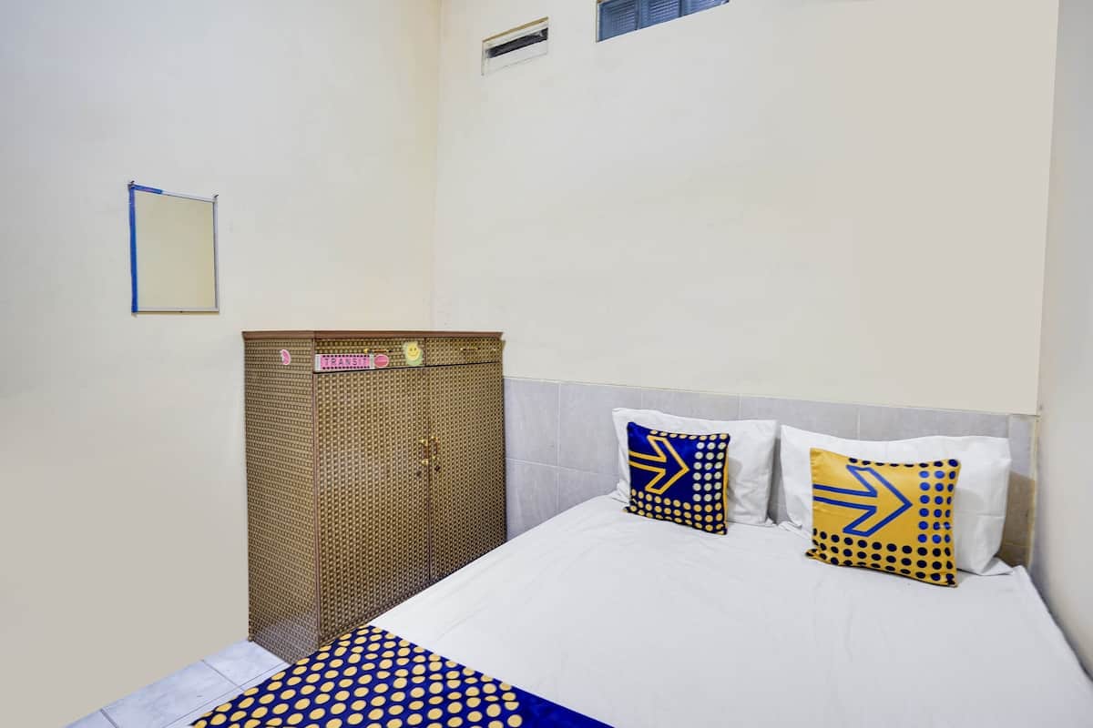 Una habitación pequeña y ordenada, con cama, dos almohadas, un espejo montado en la pared y un armario.