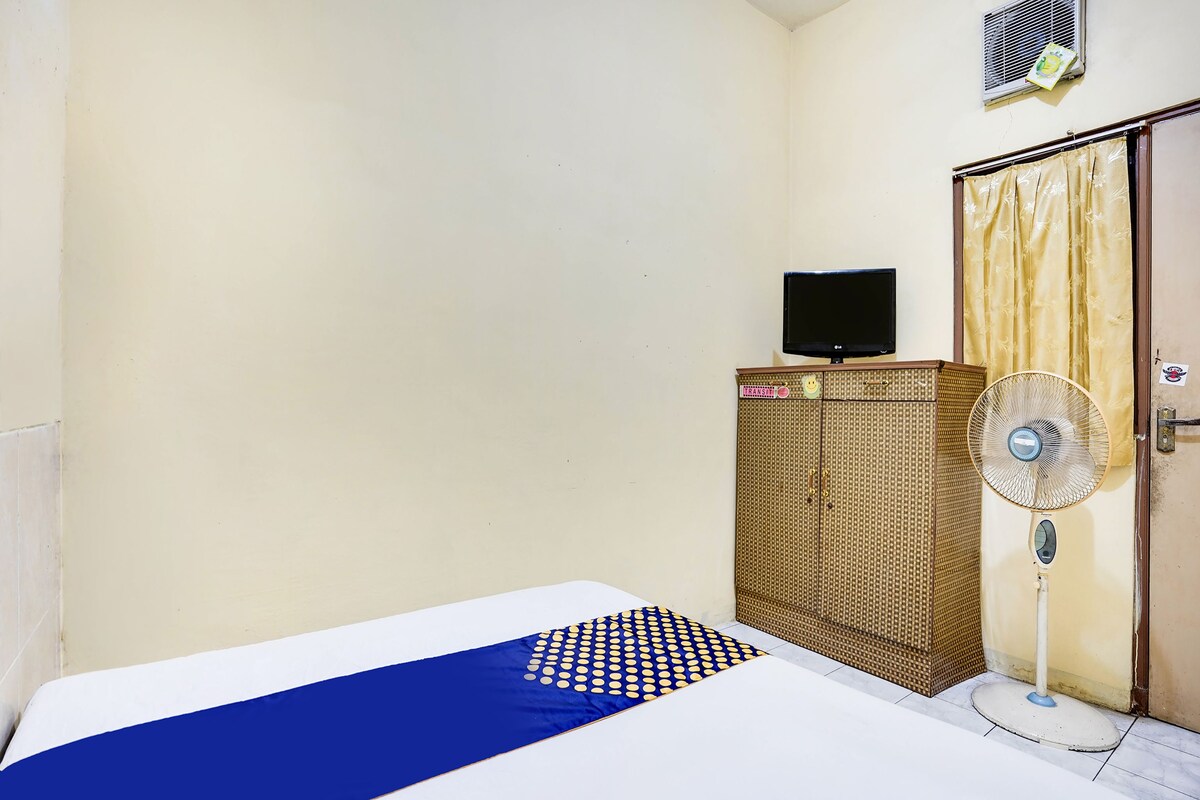 Une chambre avec un lit, une armoire, un ventilateur sur pied et un téléviseur posé sur un meuble.