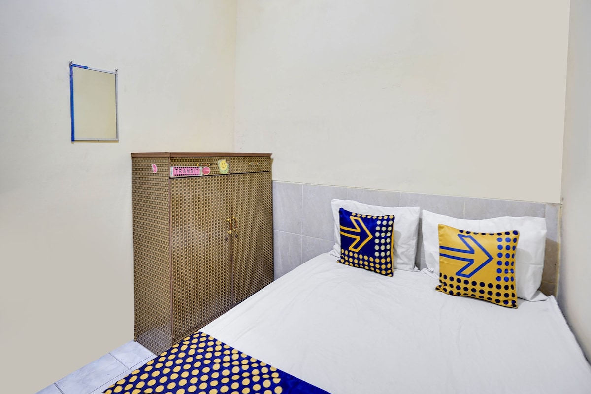 Une petite chambre avec un lit simple, un mur blanc uni, un porte-serviettes et un lit recouvert d’un drap blanc et agrémenté de deux oreillers aux motifs géométriques.