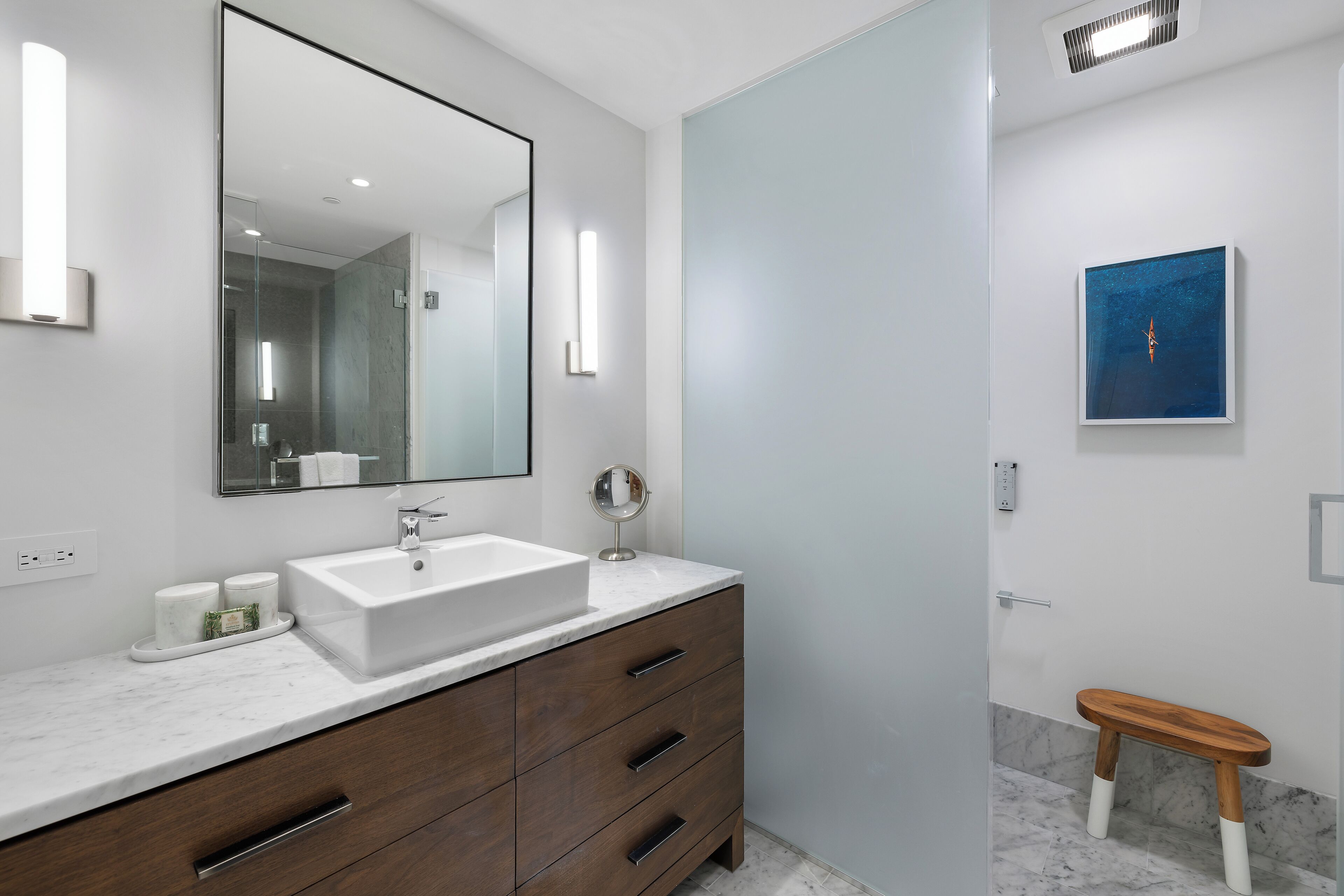 Een moderne badkamer met een witte wastafel, een houten opbergmeubel en een klein houten krukje.