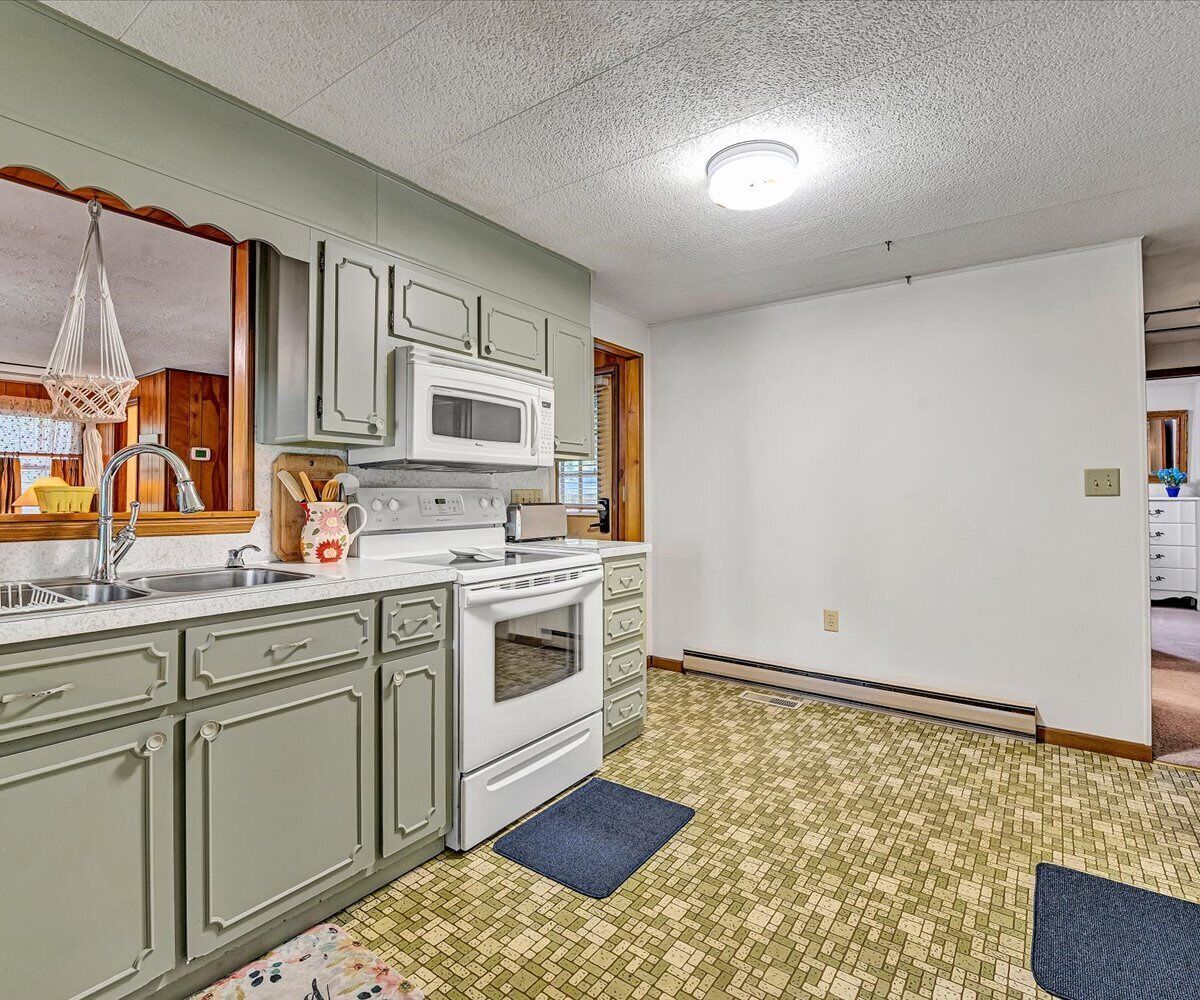 A kitchen with white appliances, green cabinets, and a tiled floor.