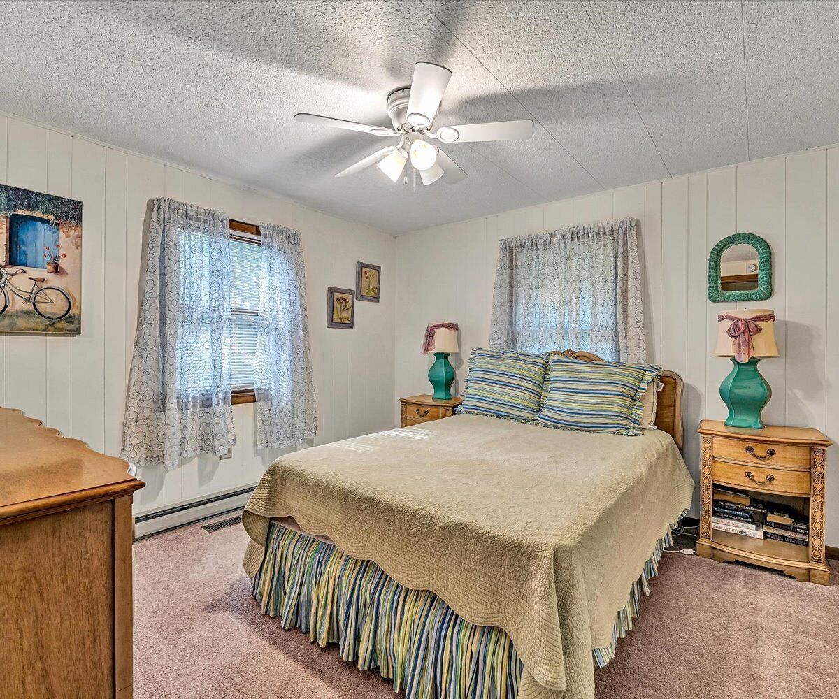 A bedroom with a bed, a ceiling fan, two nightstands, a dresser, and a window with curtains.