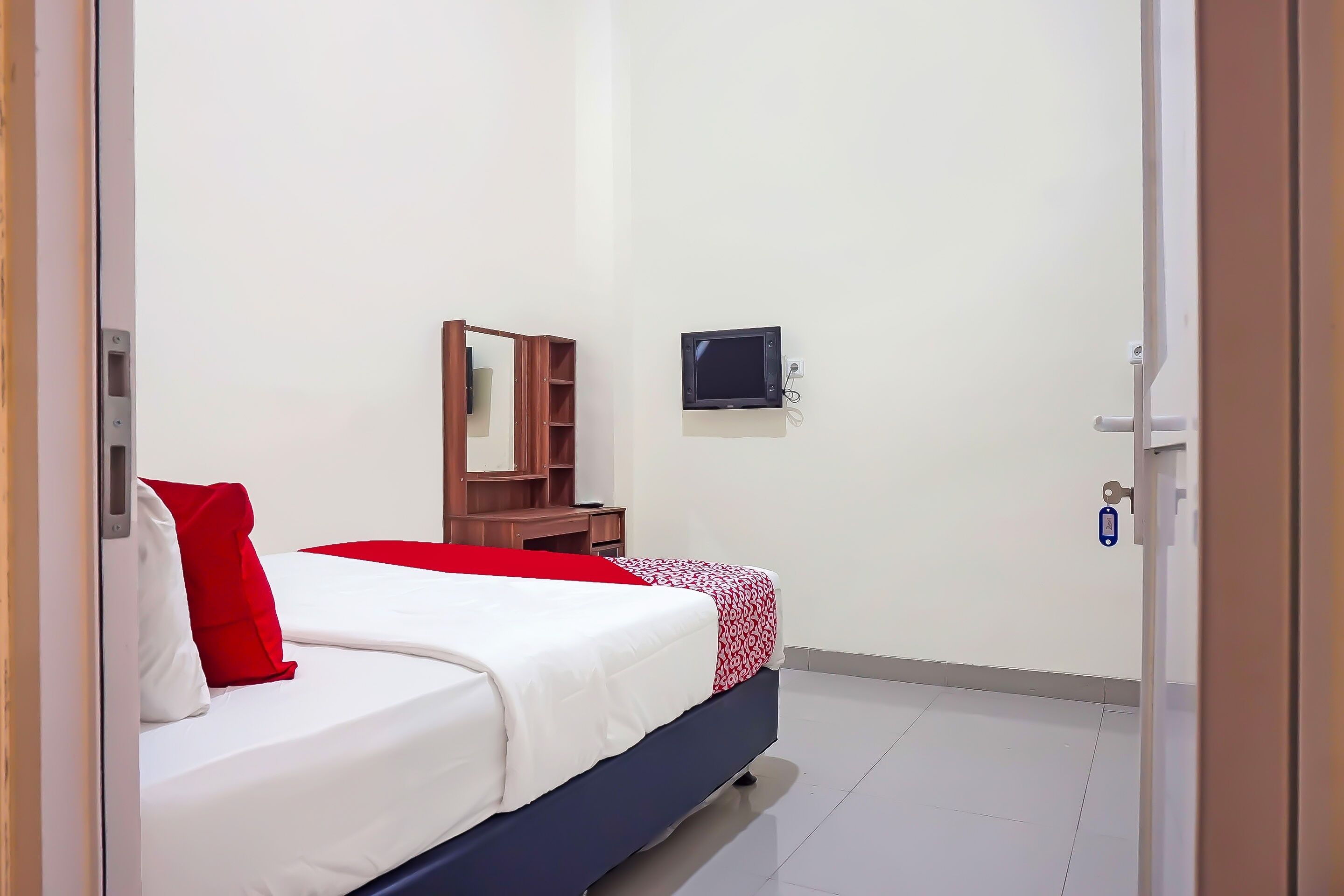 A hotel room with a bed, a desk, a chair, a television, and a door.