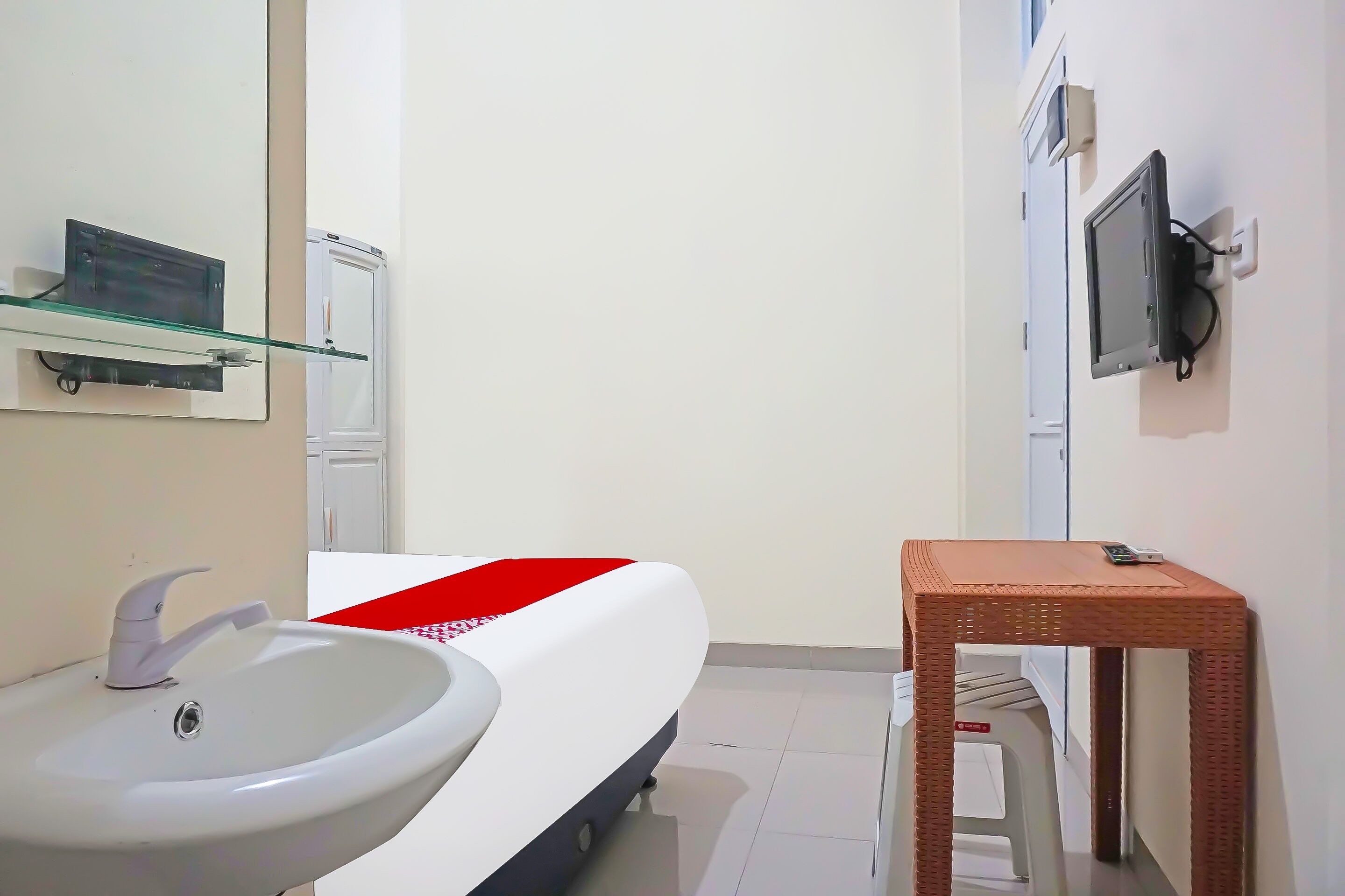 Un baño pequeño y moderno con un lavabo blanco, un estante de vidrio, una puerta blanca y una pequeña mesa de madera.