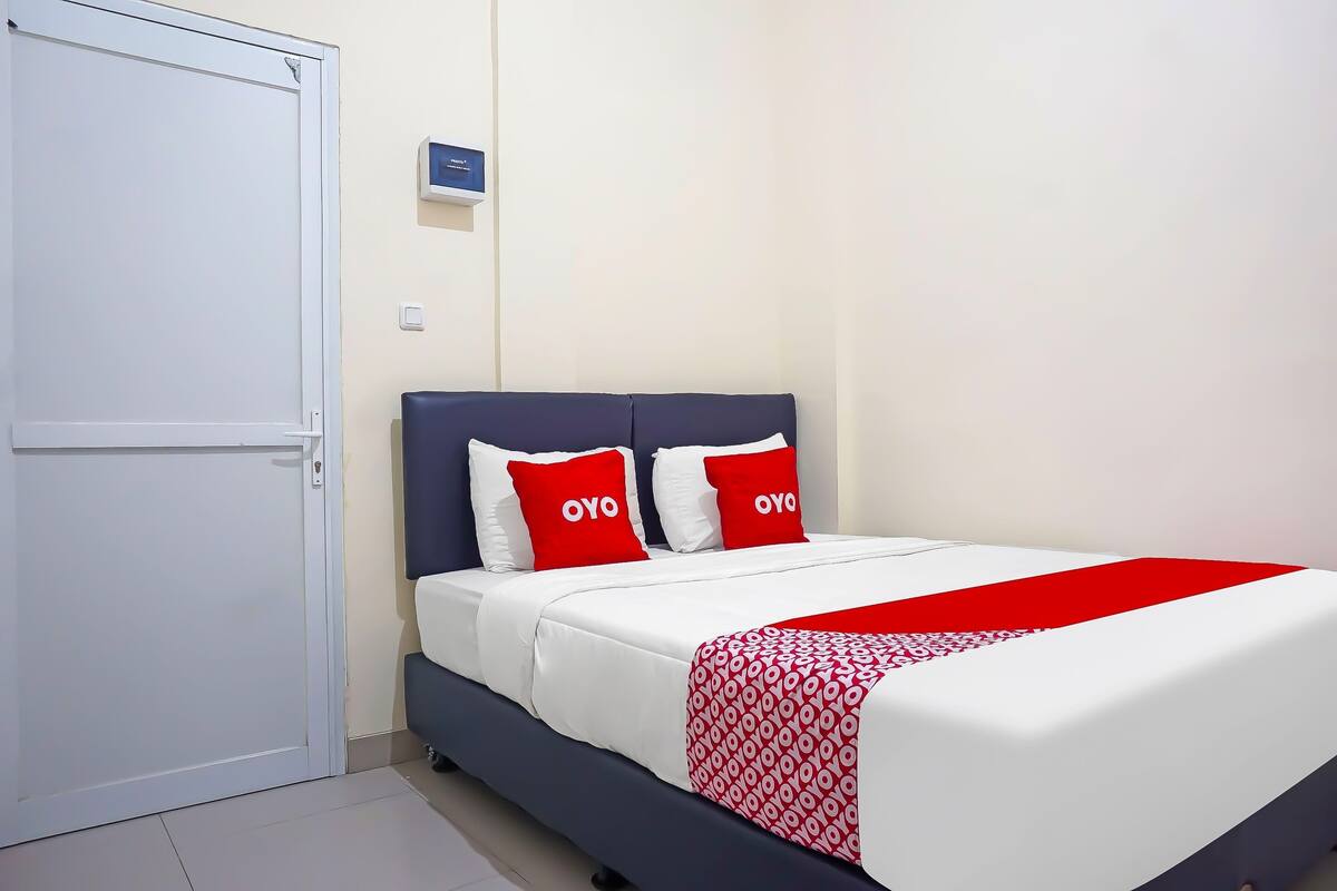 Een hotelkamer met een bed, een witte deur en een klein bord aan de muur.