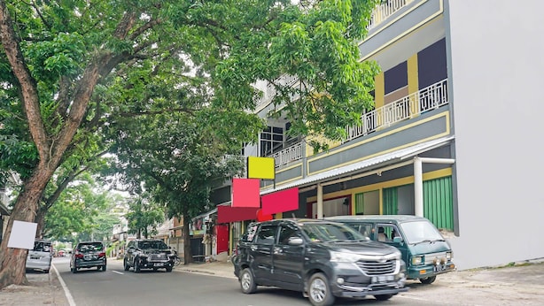 Une vue de rue avec des voitures garées, un immeuble doté de balcons et un trottoir bordé d’arbres.