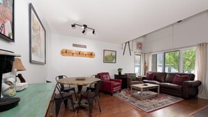 Een gezellige woonkamer met een houten salontafel, een rode leren fauteuil, een bruine leren bank en een eethoek met een ronde tafel en stoelen.