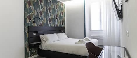 Habitación de hotel moderna con cama, escritorio, silla, televisor montado en la pared y ventana con cortinas.