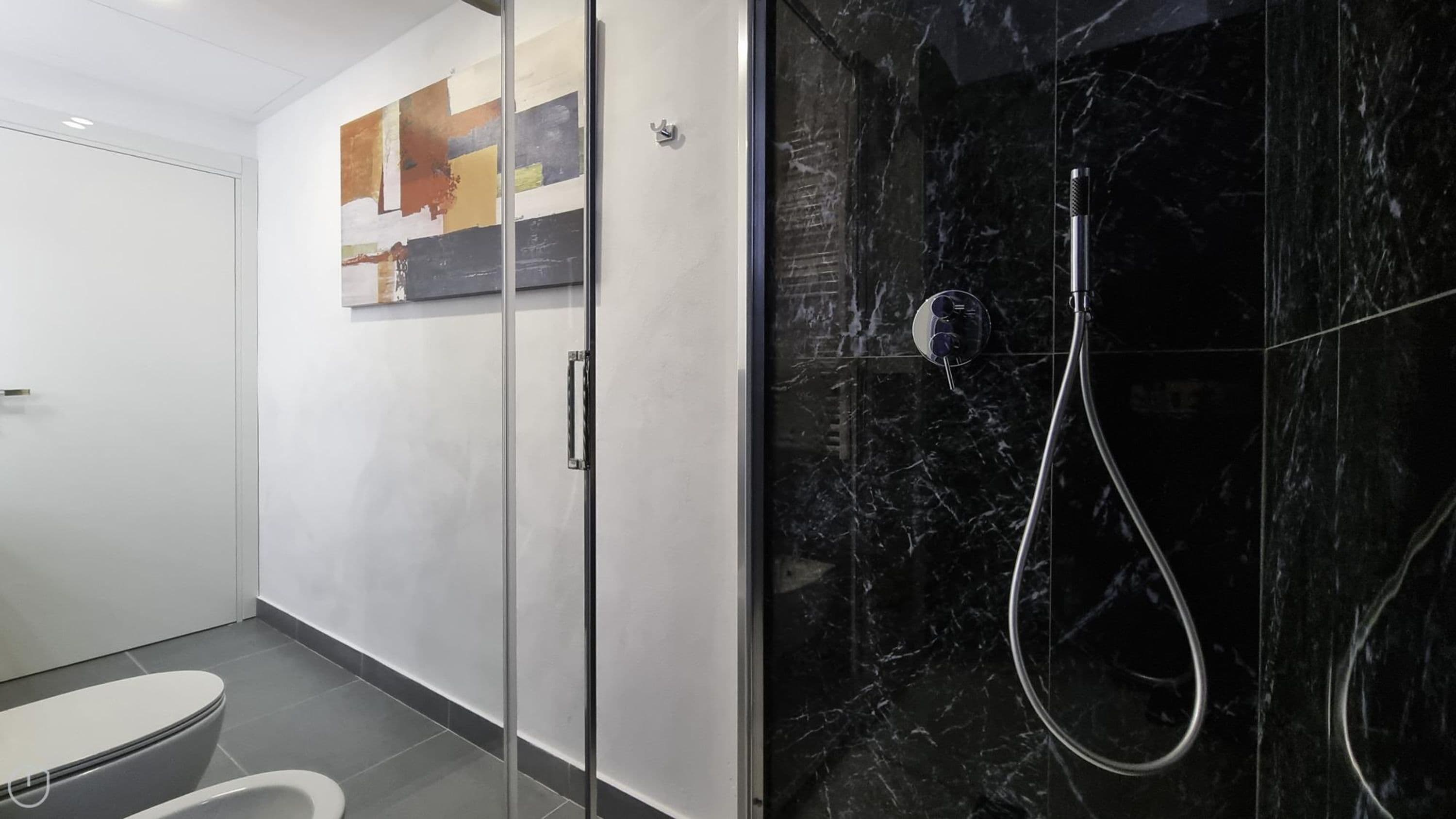 Un baño moderno con cabina de ducha de vidrio, inodoro y lavamanos empotrado.