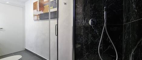 Un baño moderno con cabina de ducha de vidrio, inodoro y lavamanos empotrado.