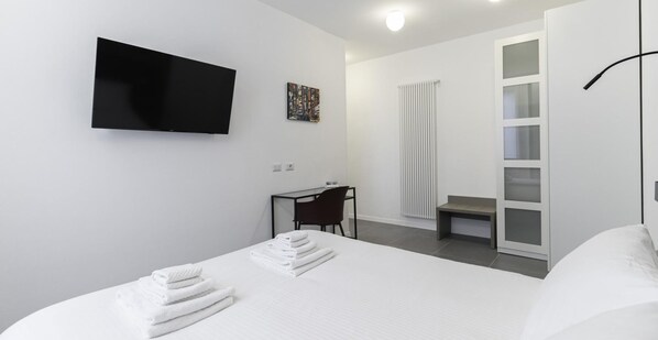 A modern hotel room with a bed, a desk, a chair, a TV, and a radiator. - Italianway Comfort - Taramelli 60 (Milan)