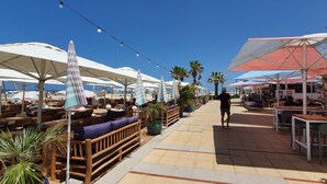 An outdoor seating area with wooden benches and tables, surrounded by umbrellas providing shade. - Ramat Yam Marine in Herzliya (Herzliya)