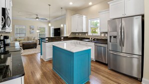 A modern kitchen with white cabinets, a blue island, stainless steel appliances, and a dining area with a sofa and coffee table.