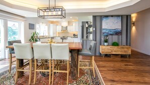 A modern kitchen with white cabinets, a wooden dining table, and a large painting on the wall. - Waterfront LUXURY Guesthouse + Spa Amenities, near Martinique Beach (Musquodoboit Harbour)