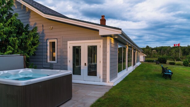 A modern house with a hot tub, a covered patio, and a well-maintained lawn. - Waterfront LUXURY Guesthouse + Spa Amenities, near Martinique Beach (Musquodoboit Harbour)