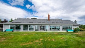 A two-story building with a grey roof and a brick chimney. It has large glass windows and doors, and two green benches in front. - Waterfront LUXURY Guesthouse + Spa Amenities, near Martinique Beach (Musquodoboit Harbour)