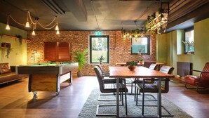 A cozy indoor space with a pool table, a wooden dining table with chairs, and a brick wall. - PHIL & MAX Hotel & Apartments  Airport (Langenhagen)