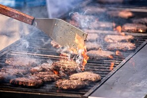A grill with multiple hamburgers cooking on it. - PHIL & MAX Hotel & Apartments  Airport (Langenhagen)