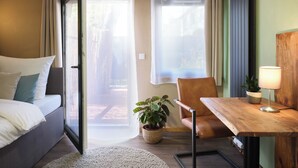 A modern hotel room with a bed, a wooden table, a chair, a potted plant, and a view through the curtains. - PHIL & MAX Hotel & Apartments  Airport (Langenhagen)