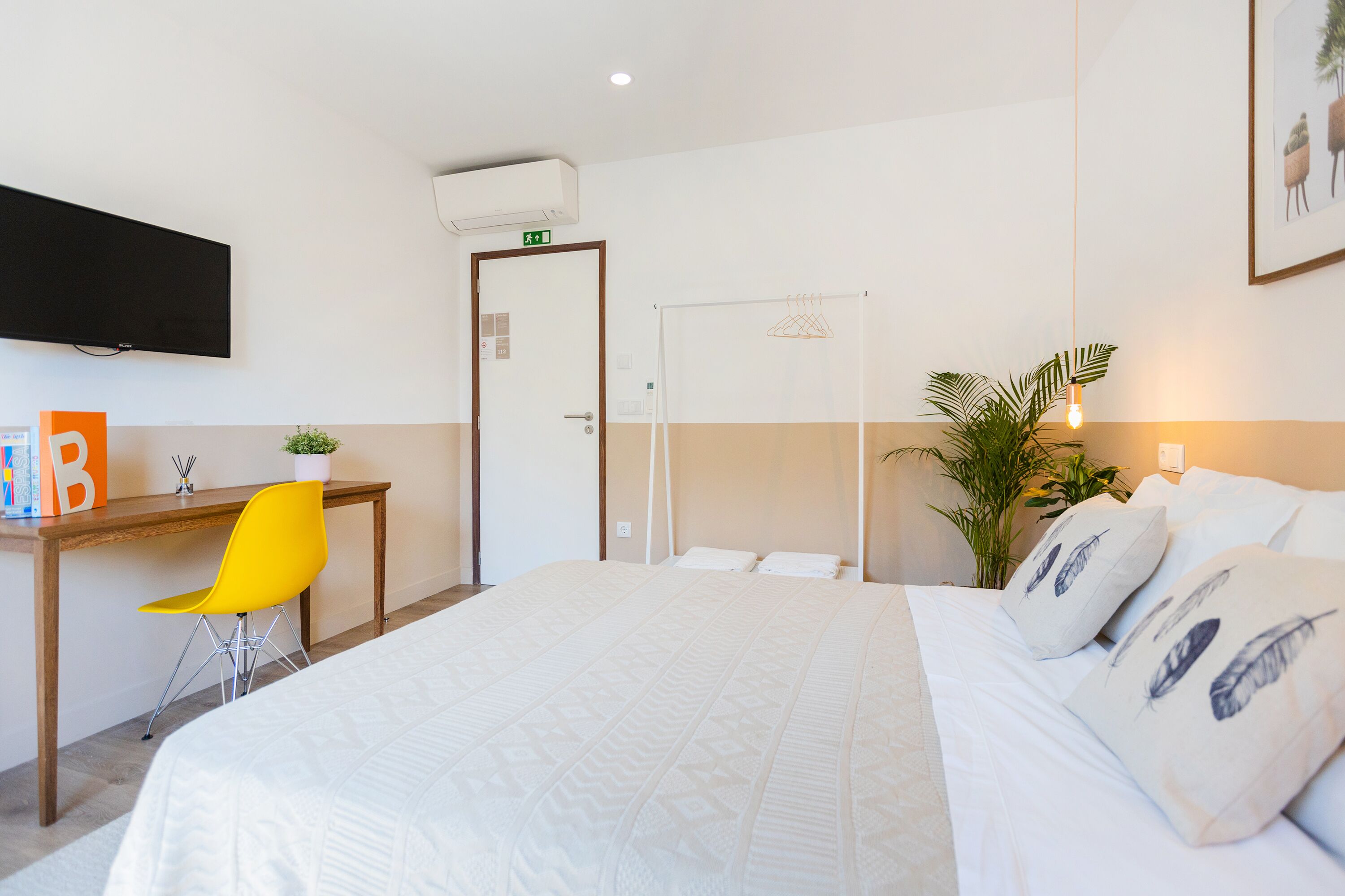 Hotellihuone, jossa on sänky, työpöytä, tuoli, televisio ja kasvi.