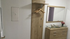 Ein Zimmer mit einem Holzschrank, einer Glastafelkommode, einem Spiegel und einer Kleiderstange.