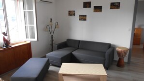 Ein Wohnzimmer mit grauem Ecksofa, einem Holztisch, einer kleinen Trommel und Wandbildern.