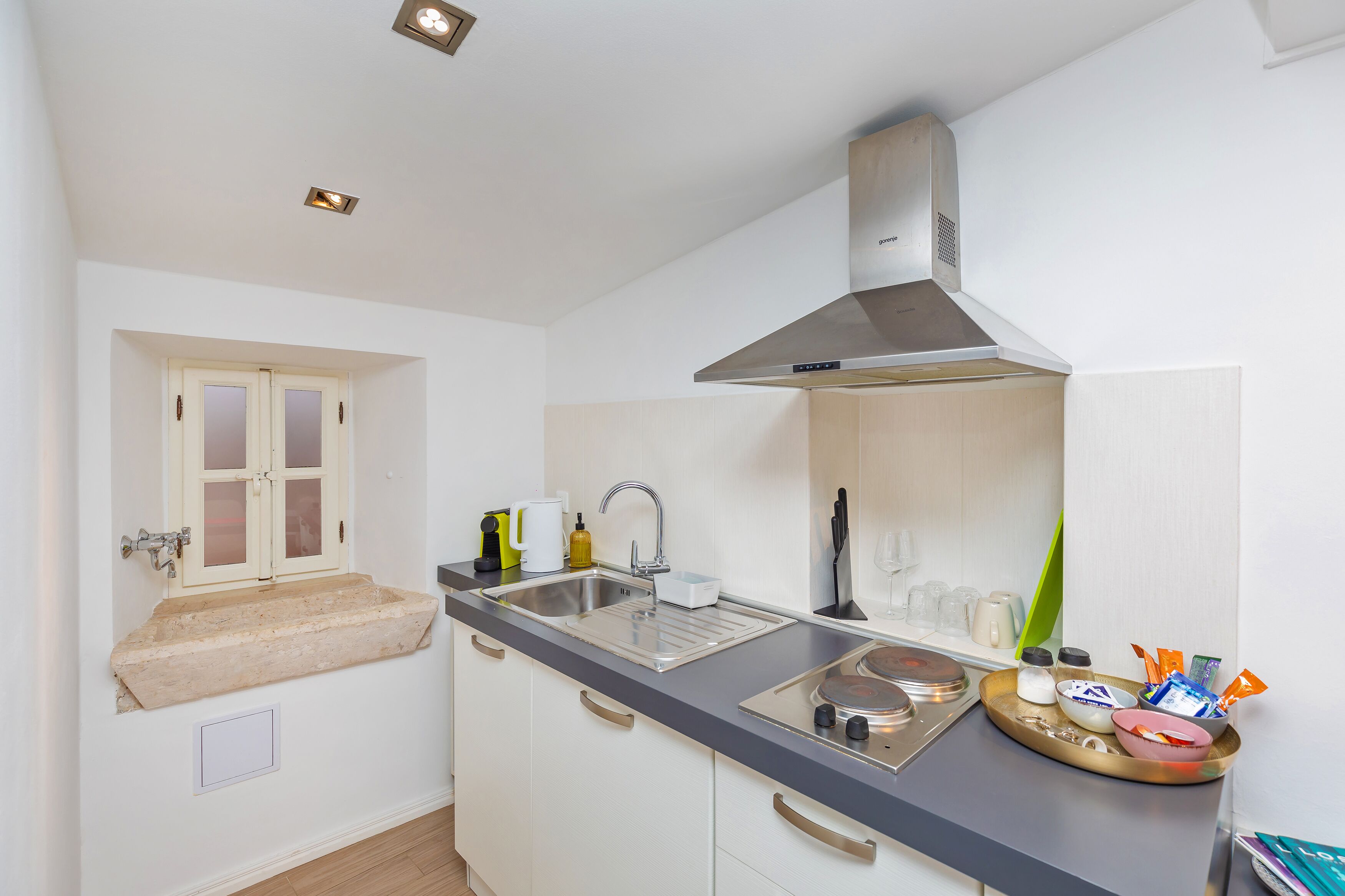 A compact kitchen with a sink, stove, and overhead ventilation hood.
