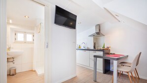 Une cuisine moderne équipée d’un téléviseur à écran plat, d’un coin repas avec une table et des chaises, et d’une salle de bain avec un lavabo et une fenêtre.