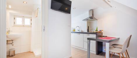 A modern kitchen with a flat-screen TV, a dining area with a table and chair, and a bathroom with a sink and window.