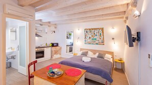 Une chambre d’hôtel de taille réduite comprenant un lit, une petite table avec un plateau, un coin cuisine et une salle de bain.