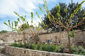 A stone wall with a tree, a lamp post, and a stone building in the background.