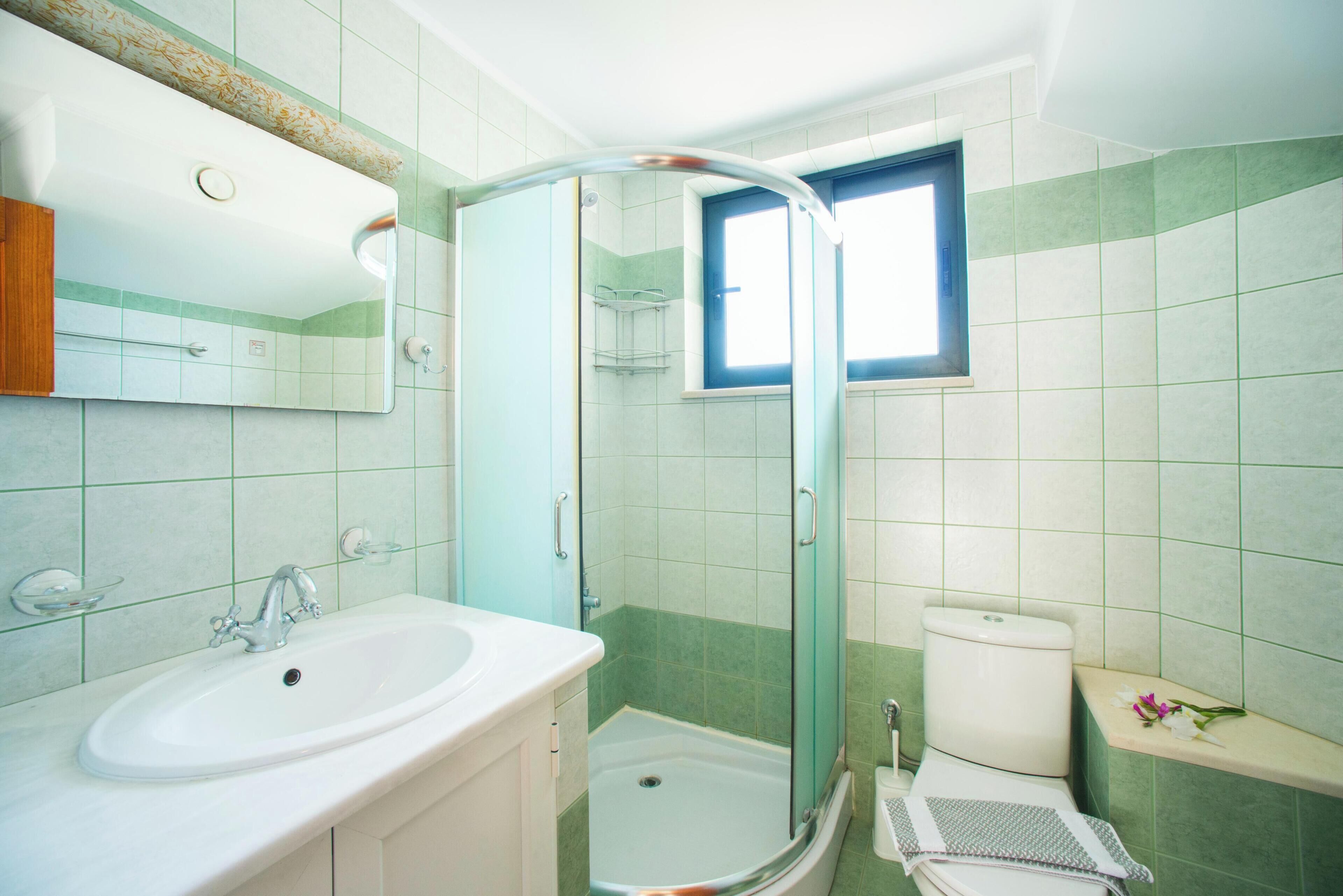 Un bagno con lavandino, specchio, doccia, WC e una finestra.