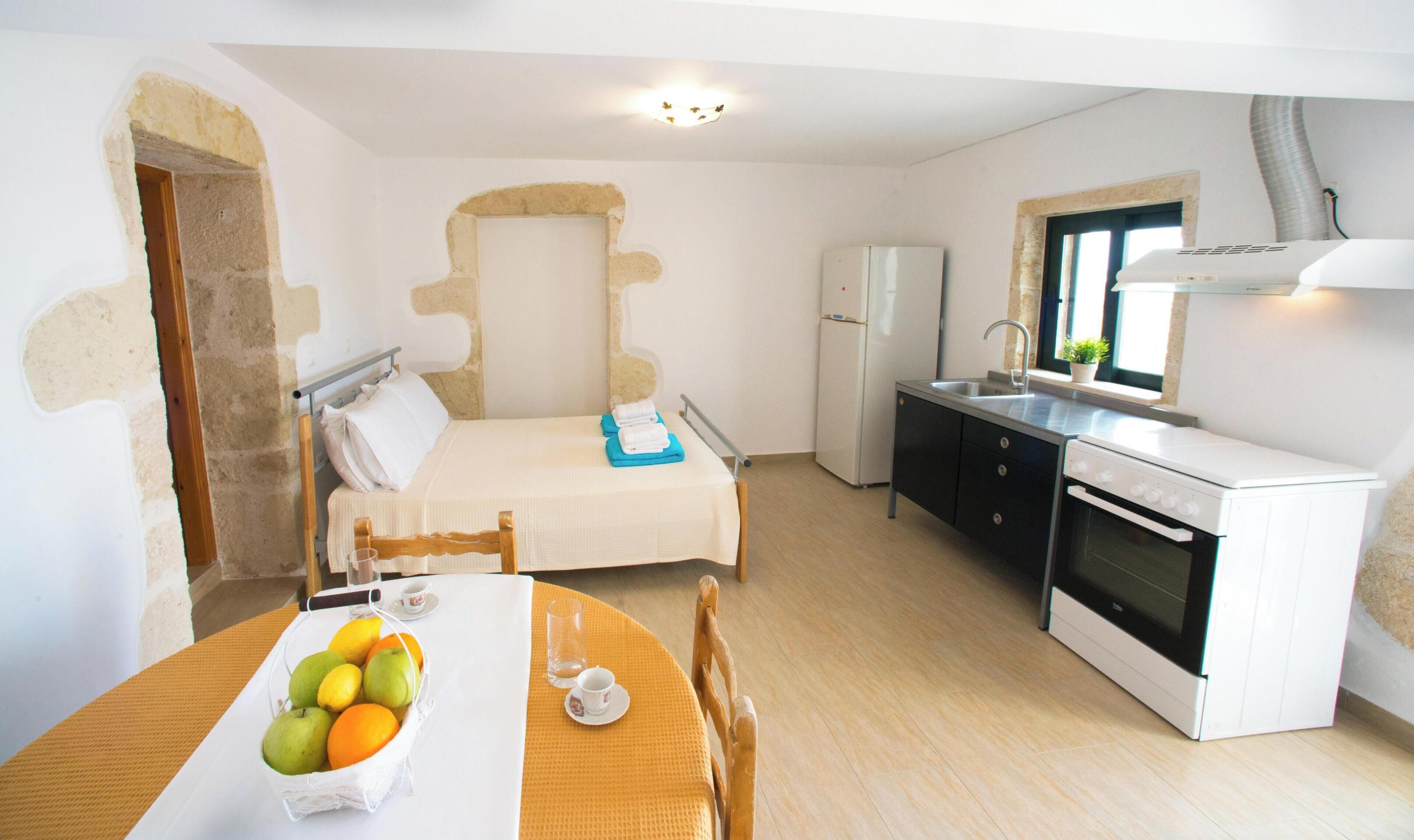A compact room with a bed, a small kitchen with a stove, and a dining area with a table set for two.