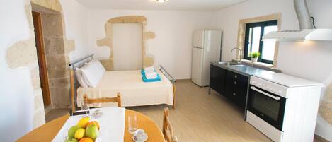 A compact room with a bed, a small kitchen with a stove, and a dining area with a table set for two.