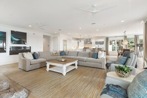 A spacious living room with a large sectional sofa, a coffee table, and a dining area with a kitchen in the background.