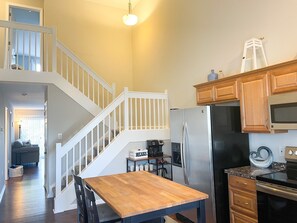 A kitchen with a wooden table, a stainless steel refrigerator, wooden cabinets, and a staircase leading to another level. - Newly Furnished Rehoboth Home Close to Everything! (Rehoboth Beach)