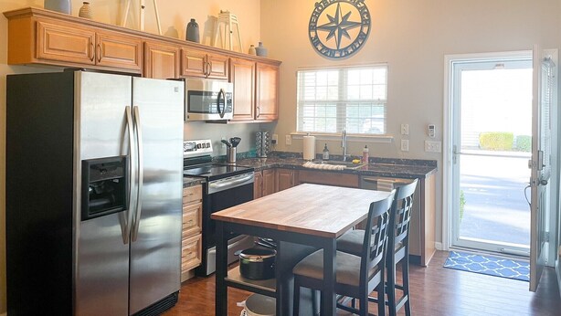 A kitchen with wooden cabinets, stainless steel appliances, a wooden dining table, and a large window.