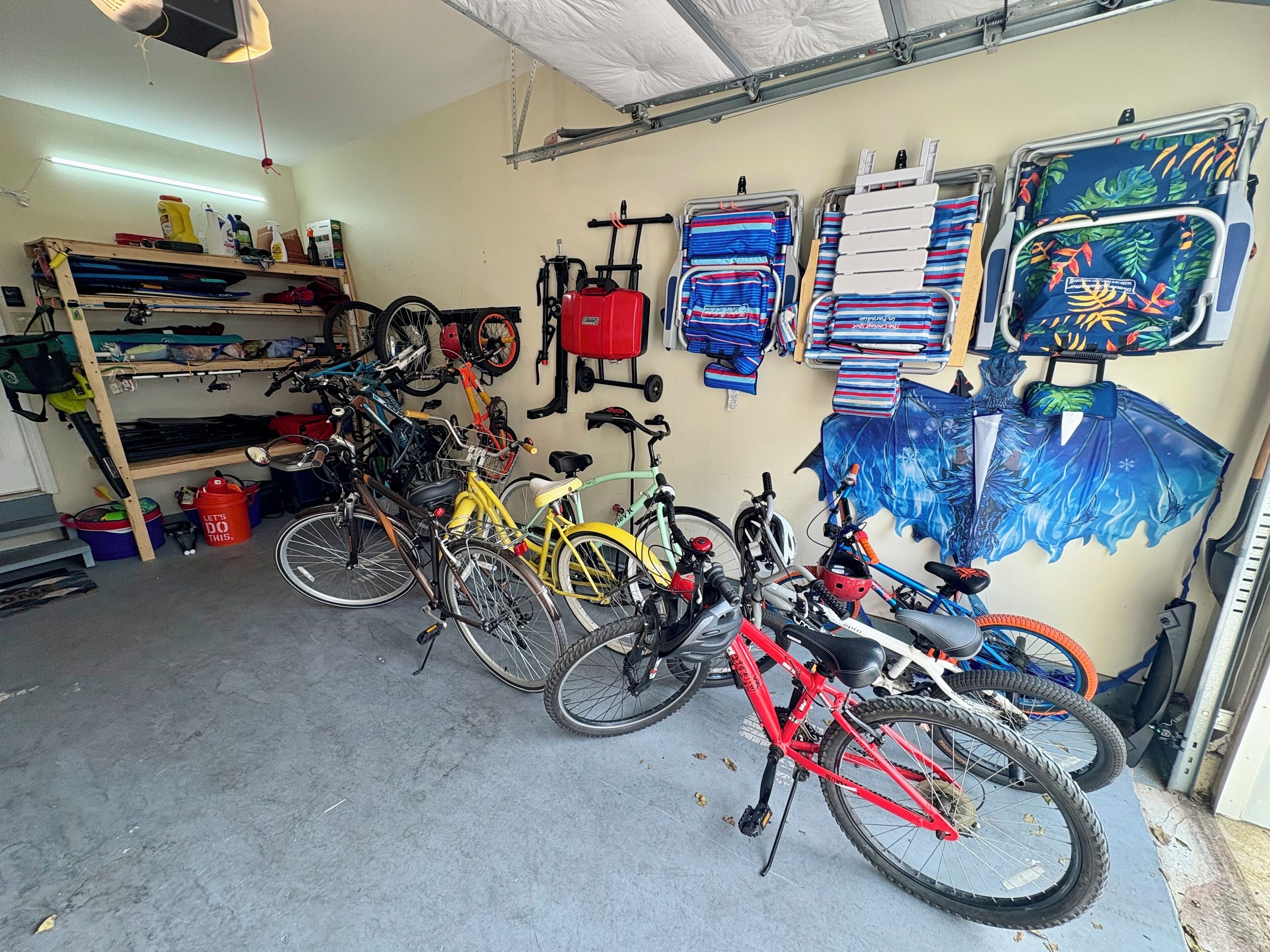A bicycle storage area with multiple bikes, a red bucket, and a wall-mounted rack with folded items.