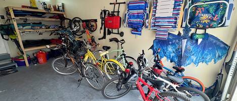 A bicycle storage area with multiple bikes, a red bucket, and a wall-mounted rack with folded items.